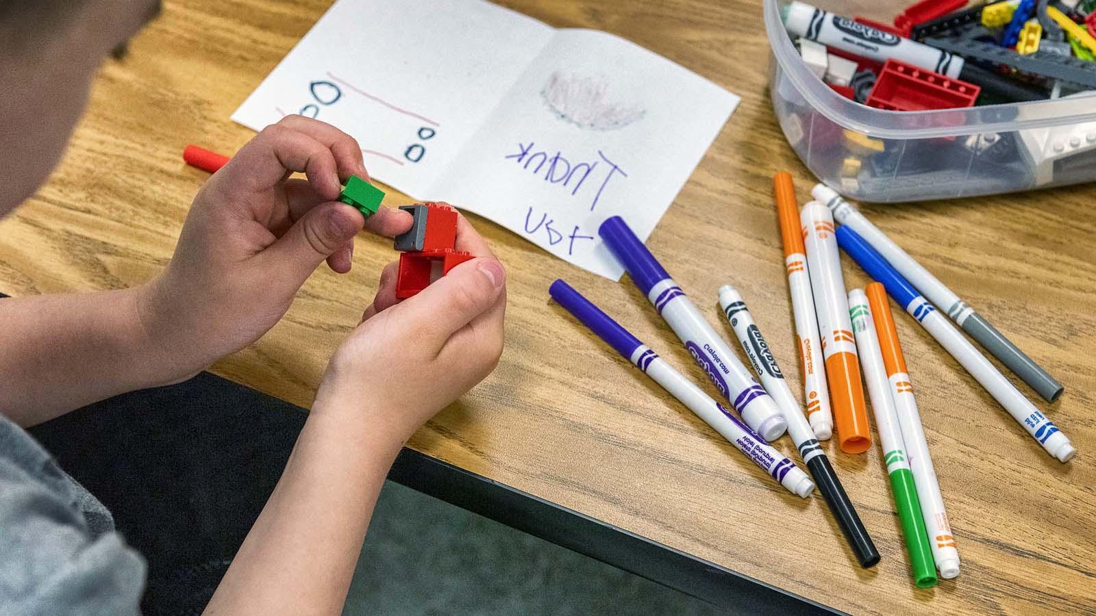 Young child playing with legos with markers and coloring sheet on table